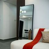 White sofa with a red throw blanket and a large mirror reflecting a room with chairs.